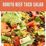 A plate of Dorito Beef Taco Salad topped with ground beef, black beans, corn, lettuce, tomatoes, shredded cheese, and guacamole. The colorful Dorito Beef Taco Salad rests on an orange napkin.