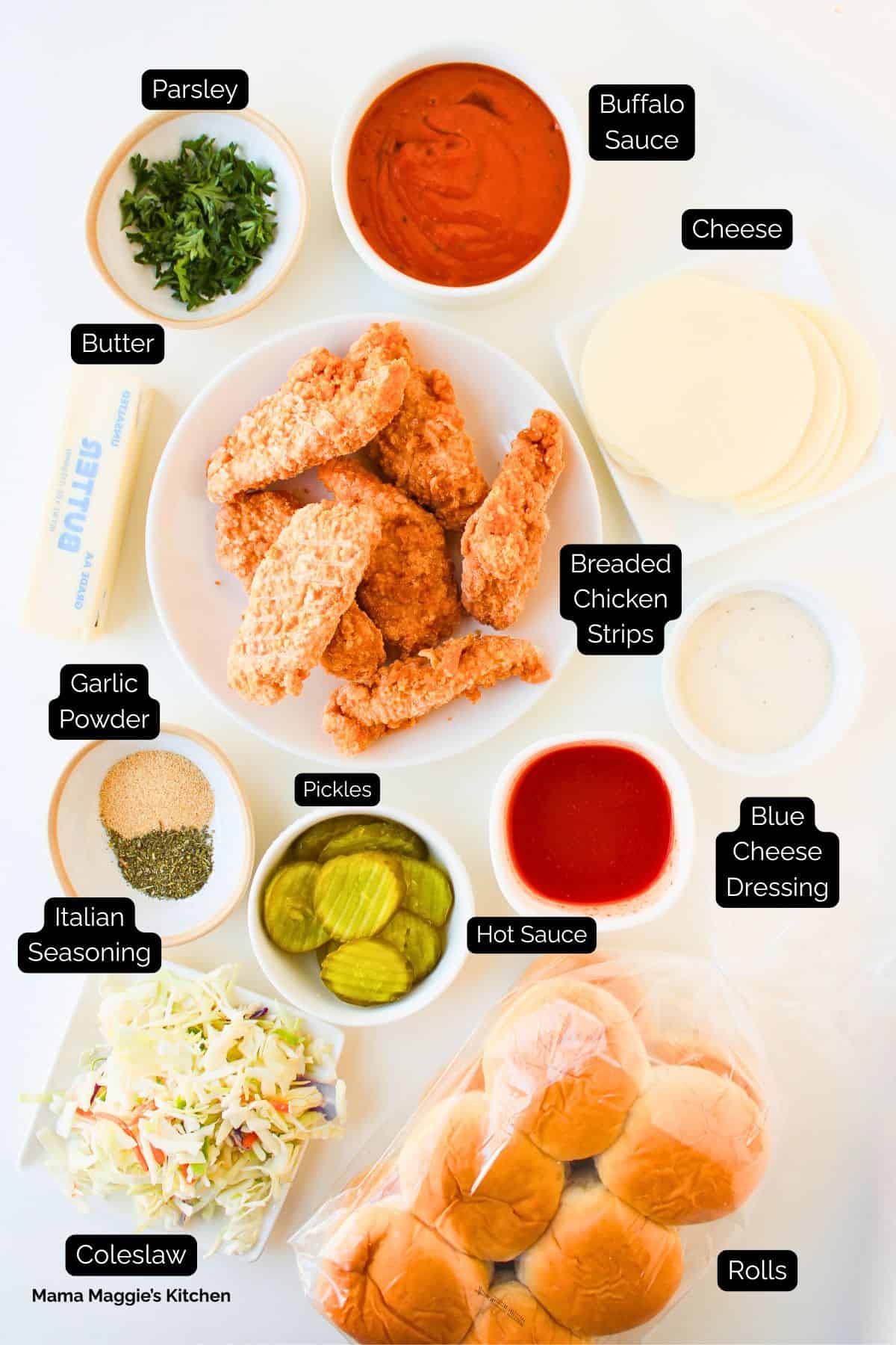 A plate of breaded chicken strips surrounded by bowls of ingredients for Buffalo Chicken Sliders—buffalo sauce, blue cheese dressing, cheese, parsley, garlic powder, Italian seasoning, hot sauce, pickles, coleslaw, butter, and a pack of rolls.