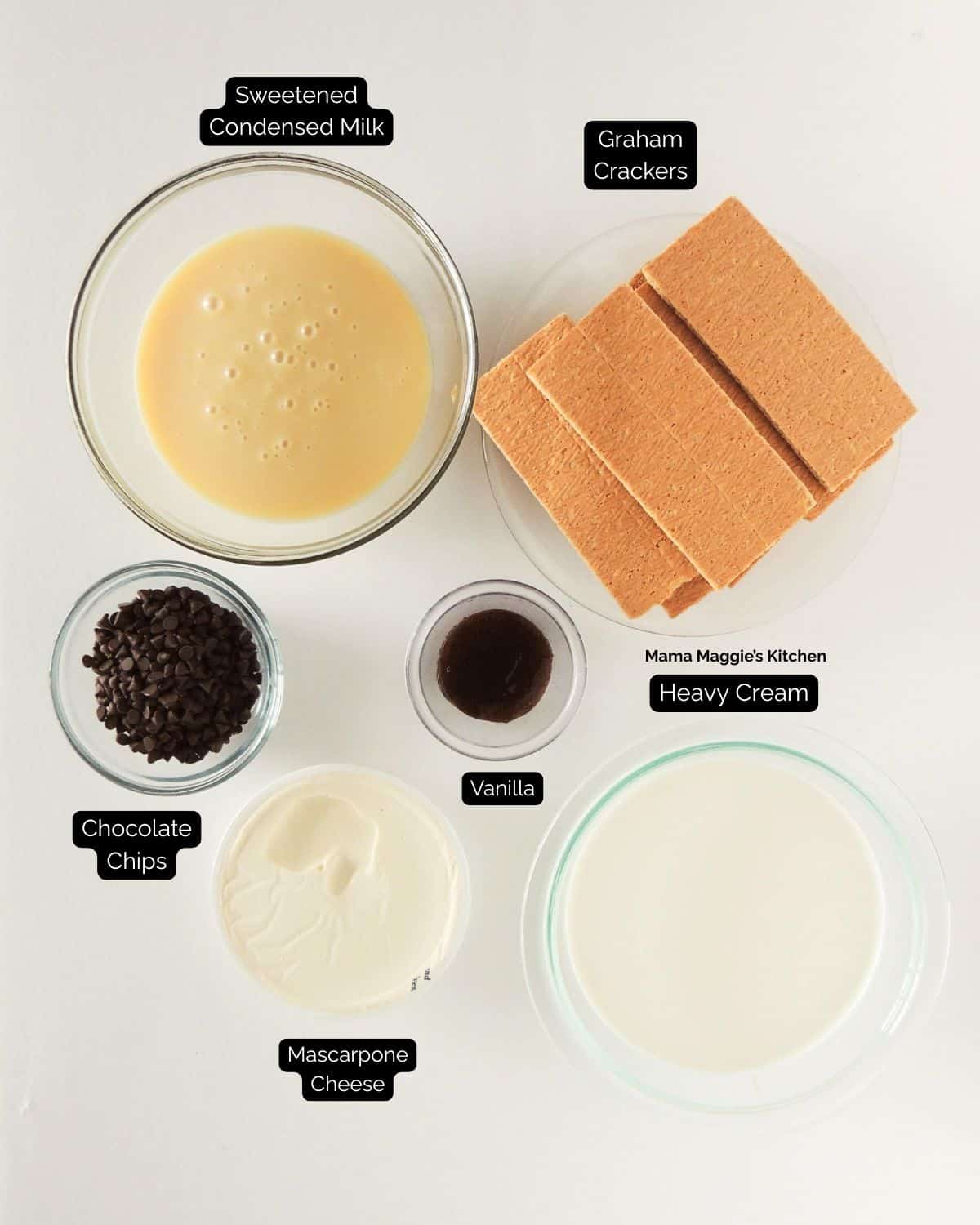 Top view of ingredients in glass bowls and plates: sweetened condensed milk, graham crackers, chocolate chips, vanilla extract, mascarpone cheese, and heavy cream—all labeled on a white background, with a bowl of chocolate chips on the wooden table nearby.