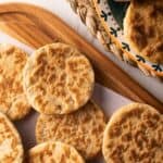Several golden-brown, round flatbreads—known as gorditas de azucar—are arranged on a wooden board and a decorative plate, showing a rustic, textured surface.