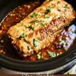 Pork loin garnished with herbs sits in a slow cooker, surrounded by a spicy, saucy mixture. Text reads “Slow Cooker Honey Lime Chipotle Pork Loin.”.