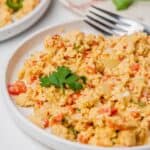 Huevos a la Mexicana—scrambled eggs with diced tomatoes, onions, and herbs—are served on a white plate and garnished with a sprig of parsley. A fork and cilantro are in the background.
