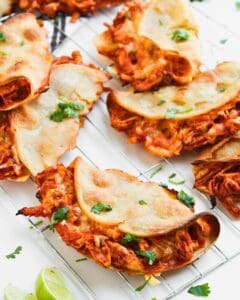 Several crispy baked chicken tacos garnished with cilantro on a wire cooling rack, with a lime wedge nearby.