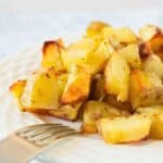A pile of crispy baked Mexican potatoes on a white plate with a fork in the foreground.