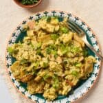 Migas con huevo served topped with green onions on a patterned plate, with a fork and a small bowl of chopped cilantro nearby.