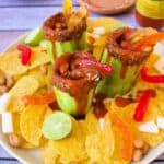 Three Pepinos Locos cucumber cups filled with chamoy sauce, peanuts, and gummy candies, served on a platter with tortilla chips, lime wedges, and jicama pieces.